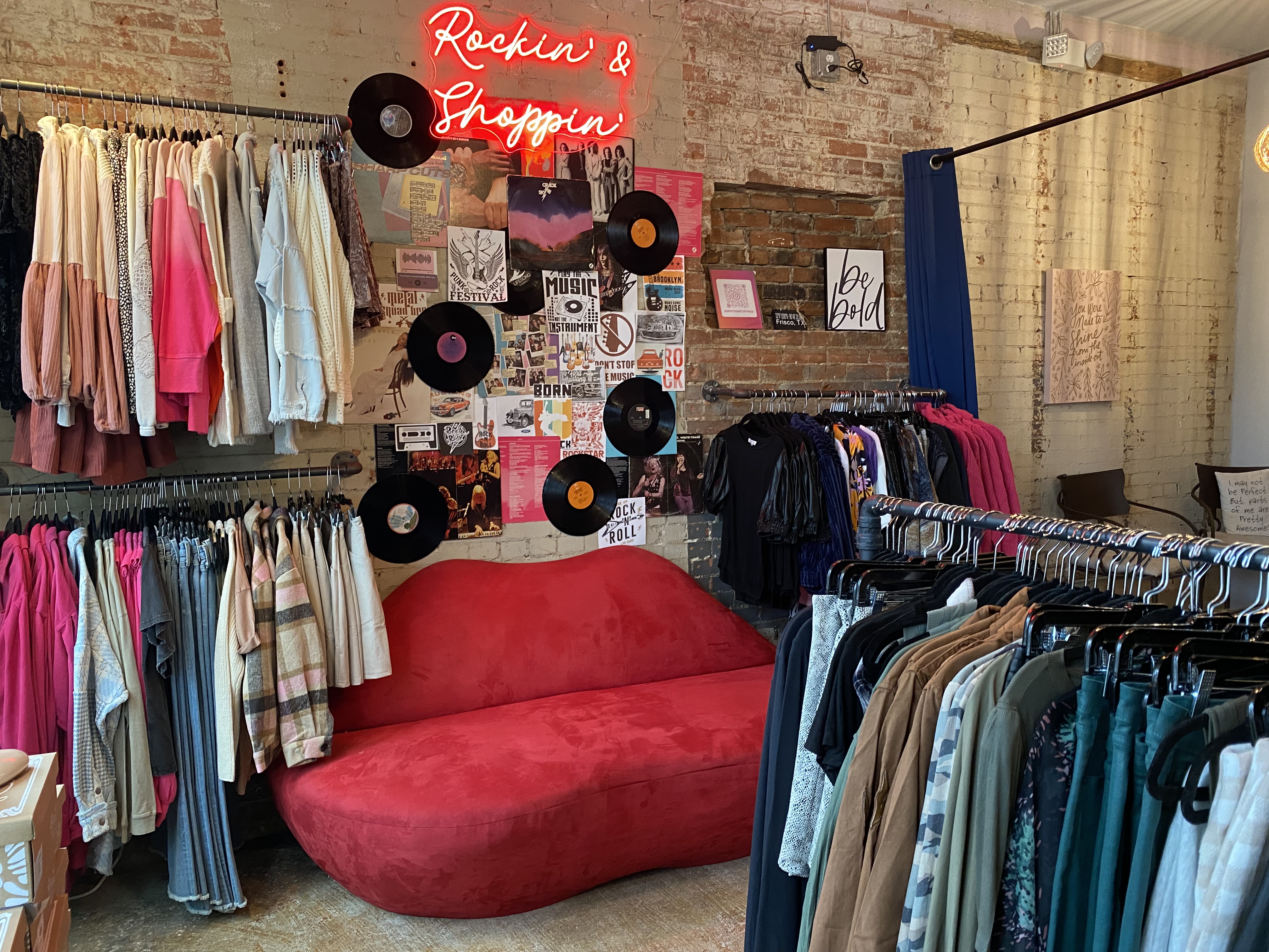 a red couch shaped like lips between clothing racks at a boutique